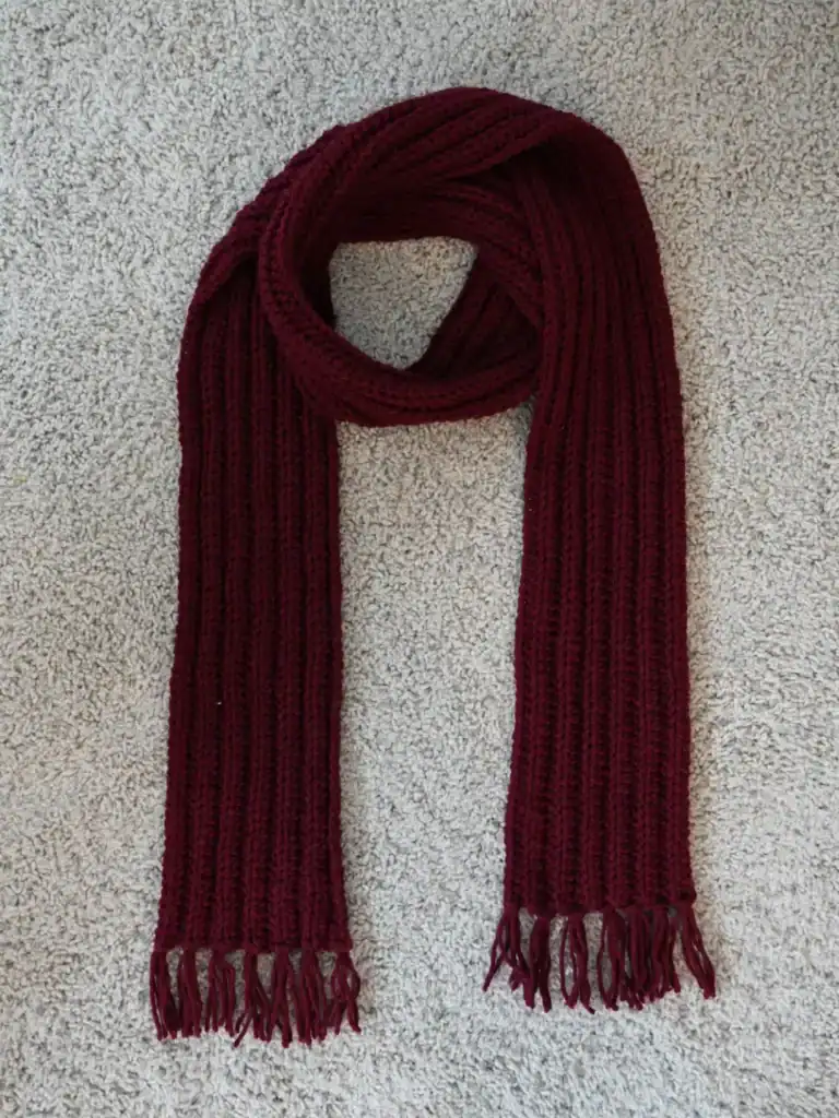 Knitted burgundy crochet scarf with fringed ends, cozy winter accessory, perfect for chilly weather.