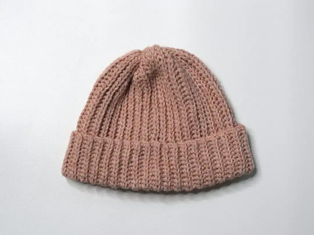 Close-up of a cozy, pink, hand-crocheted knit beanie hat on a plain white background.