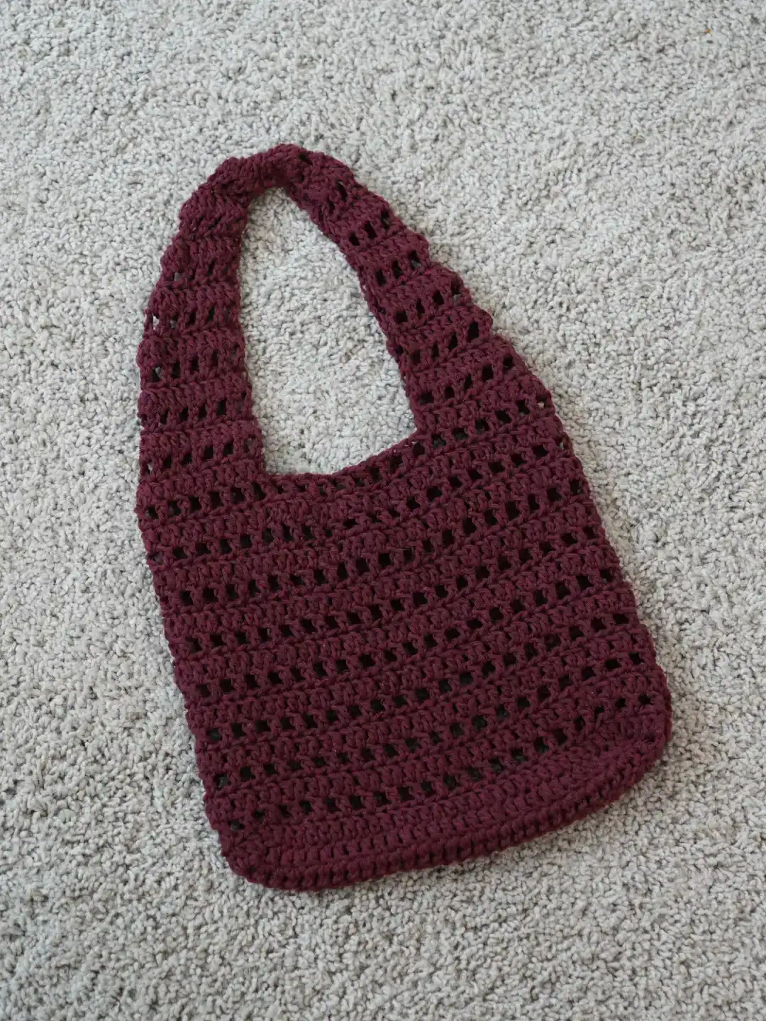 Handmade crochet tote bag in deep burgundy, crafted with soft yarn and open stitch design, perfect for everyday use.
